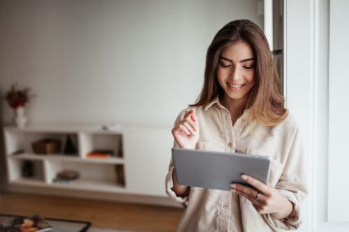 Smiling pretty young asian lady in casual use tablet for control smart home, enjoy study and work